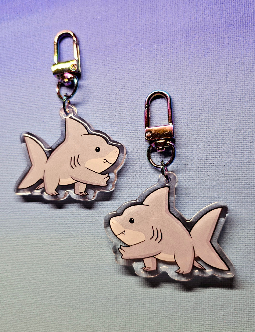 Two shark-shaped Jeff the Land Shark keychains on a light purple-to-blue gradient background